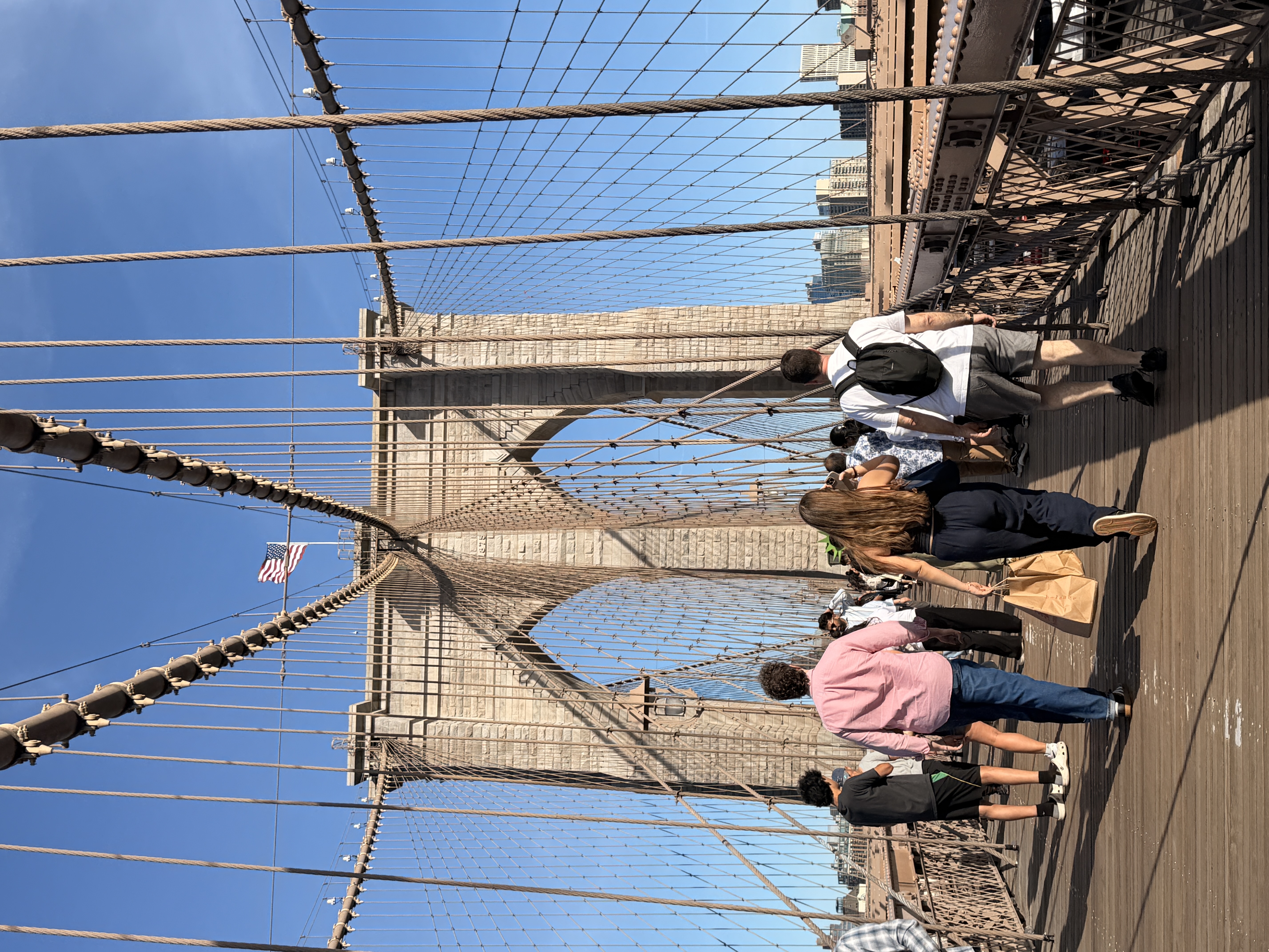 Pedestrians crossing the Brooklyn Bridge under an American flag