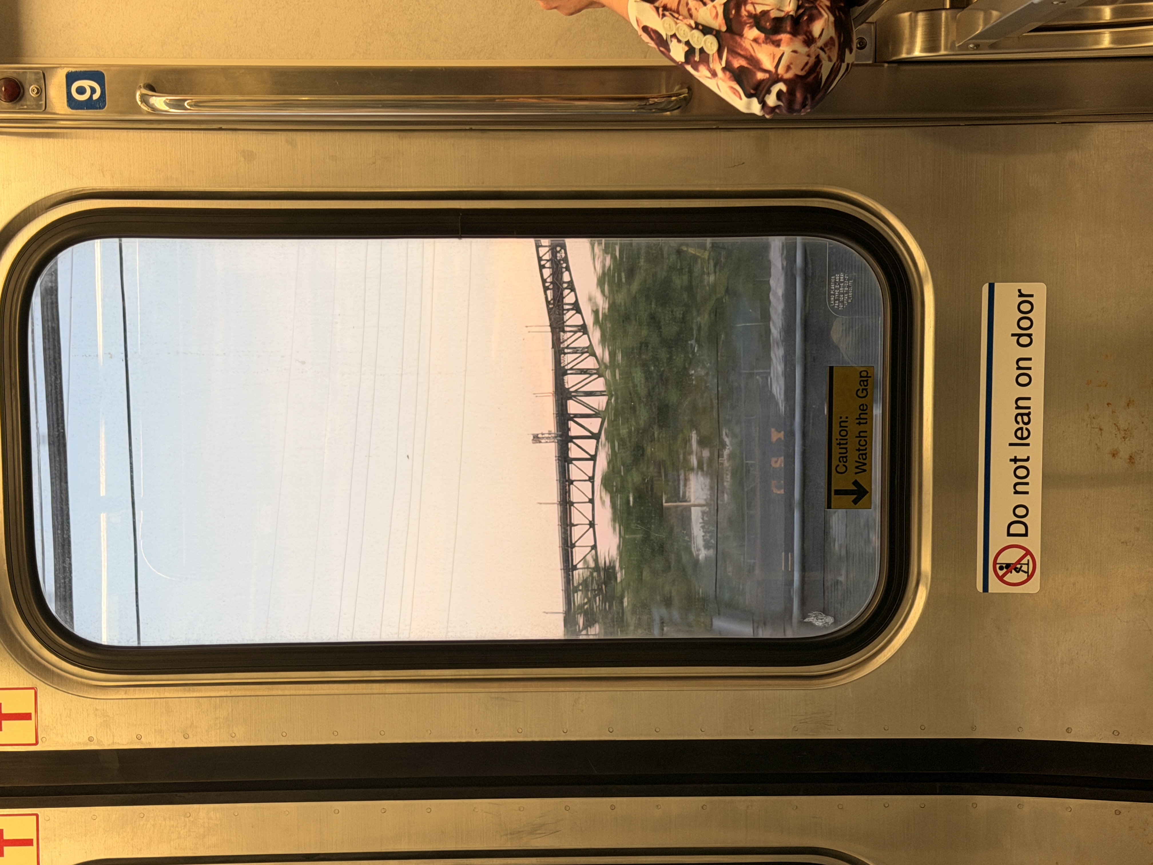 Subway car window framing a steel bridge at dusk